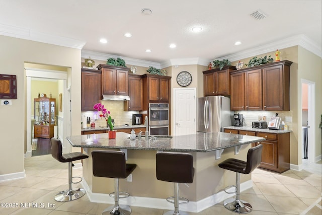 kitchen featuring light tile patterned floors, a center island with sink, a breakfast bar, and appliances with stainless steel finishes