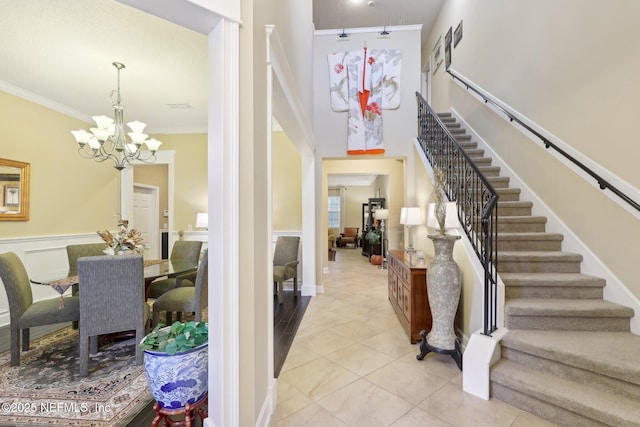 tiled entrance foyer featuring crown molding, an inviting chandelier, and a high ceiling