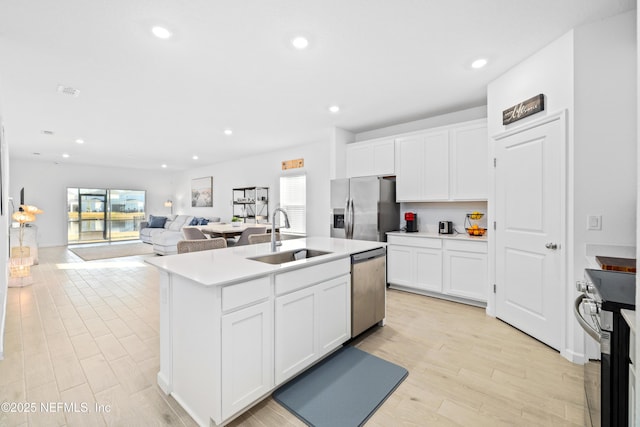 kitchen featuring sink, light hardwood / wood-style flooring, white cabinetry, stainless steel appliances, and an island with sink