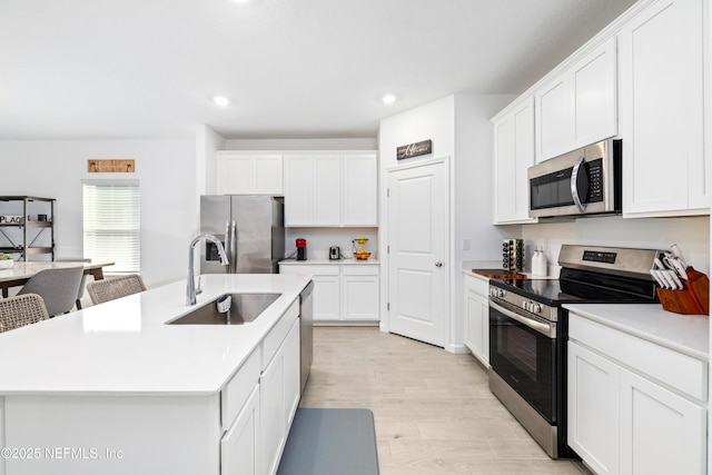 kitchen with white cabinetry, appliances with stainless steel finishes, sink, and a center island with sink