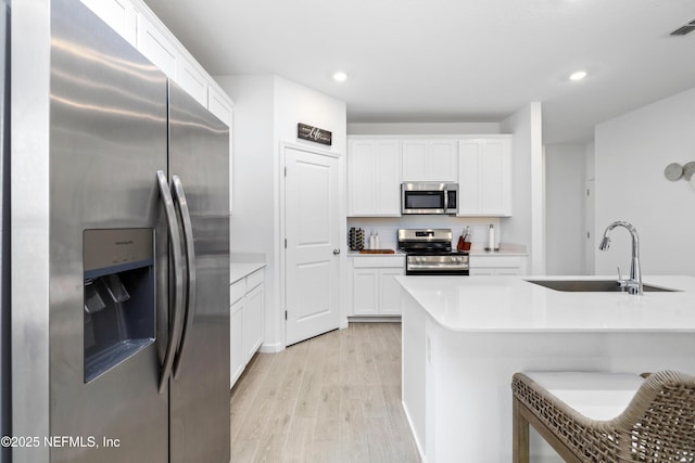 kitchen with a breakfast bar, sink, white cabinetry, stainless steel appliances, and light hardwood / wood-style floors