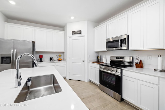 kitchen with stainless steel appliances, sink, white cabinets, and light hardwood / wood-style flooring