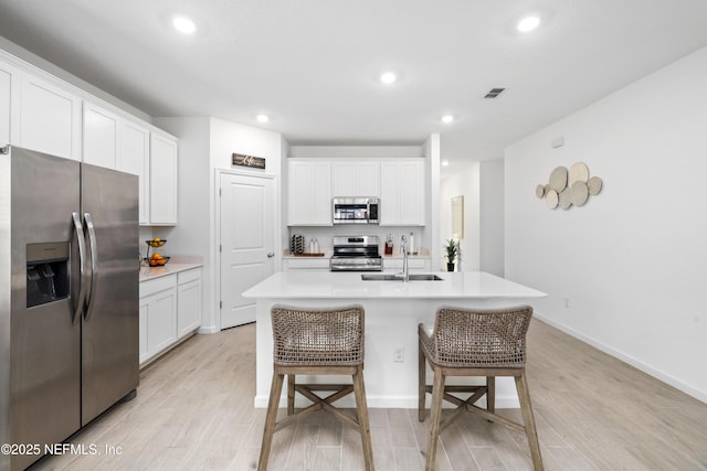 kitchen with appliances with stainless steel finishes, white cabinetry, an island with sink, sink, and light hardwood / wood-style flooring