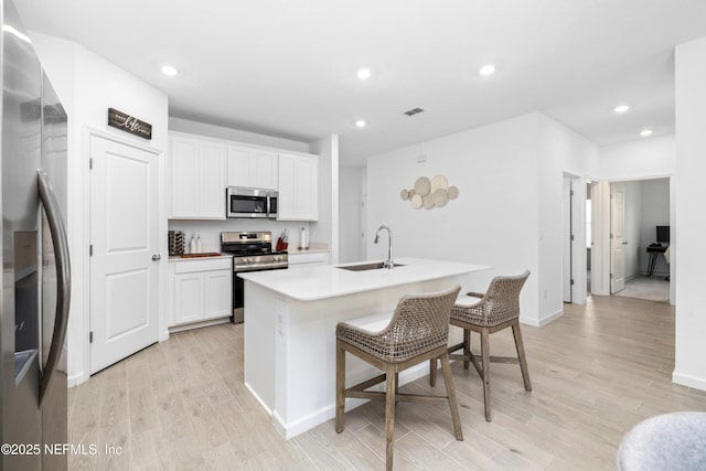 kitchen featuring sink, a breakfast bar area, appliances with stainless steel finishes, white cabinetry, and an island with sink