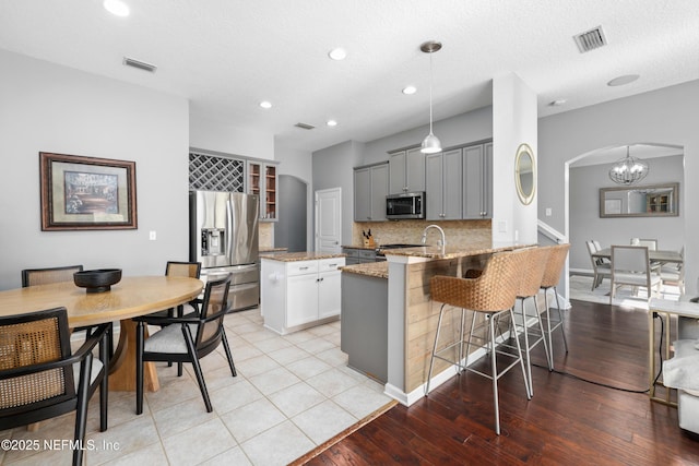 kitchen with gray cabinetry, light stone counters, tasteful backsplash, hanging light fixtures, and appliances with stainless steel finishes