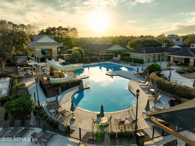 pool at dusk featuring a patio area and a water slide