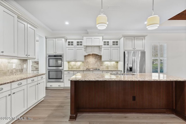 kitchen featuring appliances with stainless steel finishes, ornamental molding, light stone counters, sink, and decorative light fixtures