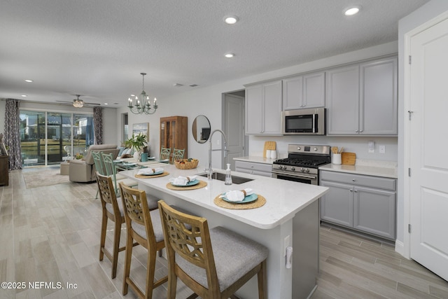 kitchen with appliances with stainless steel finishes, hanging light fixtures, gray cabinetry, and a kitchen island with sink