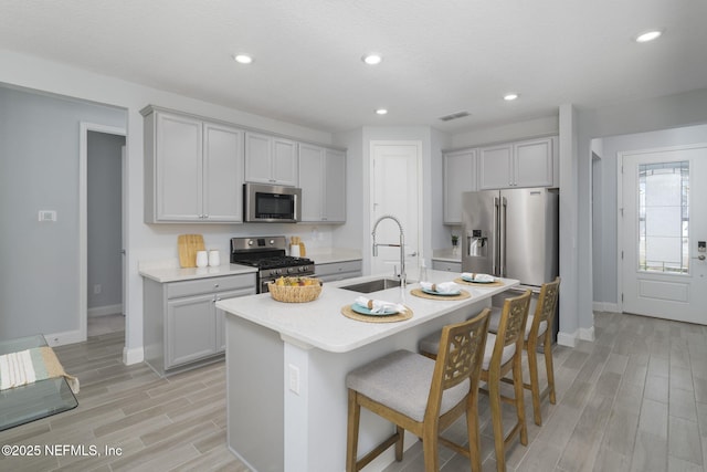 kitchen with a kitchen island with sink, stainless steel appliances, a kitchen bar, sink, and light hardwood / wood-style flooring