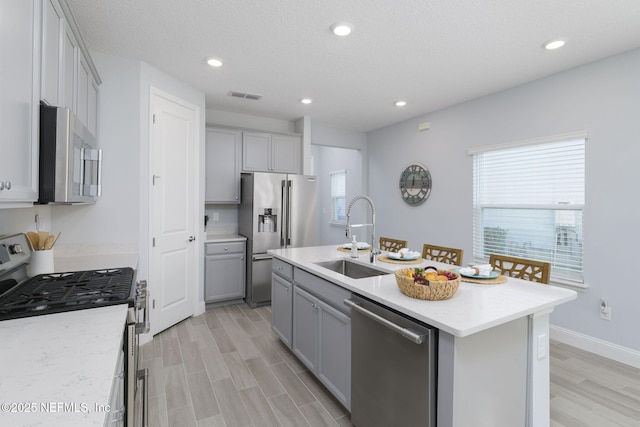 kitchen featuring sink, gray cabinets, an island with sink, and appliances with stainless steel finishes