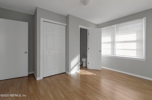 unfurnished bedroom with connected bathroom, a closet, light wood-type flooring, and a textured ceiling