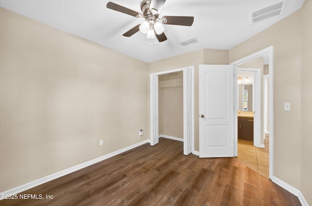 unfurnished bedroom with ceiling fan, a textured ceiling, dark hardwood / wood-style flooring, and a closet