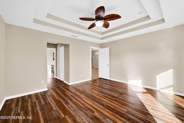 unfurnished room featuring dark wood-type flooring, ceiling fan, and a tray ceiling