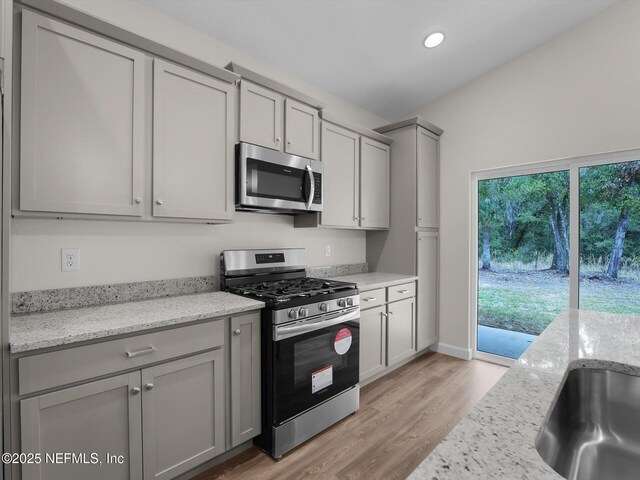 kitchen featuring appliances with stainless steel finishes, sink, gray cabinets, light stone counters, and light hardwood / wood-style flooring