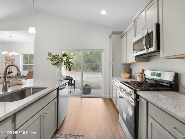 kitchen with appliances with stainless steel finishes, sink, hanging light fixtures, vaulted ceiling, and light stone counters