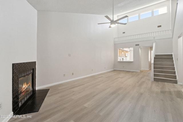 unfurnished living room with ceiling fan, plenty of natural light, a high ceiling, and a tile fireplace