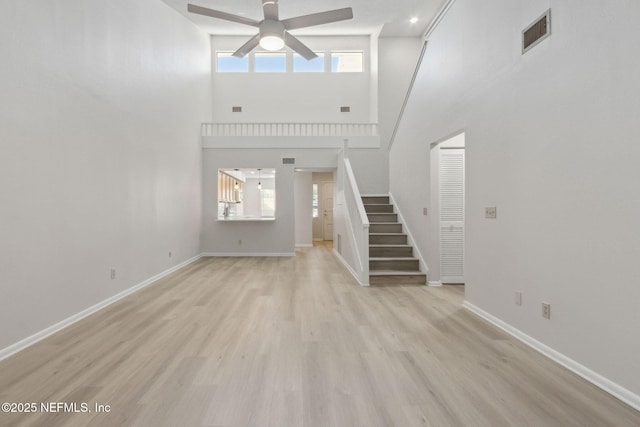 unfurnished living room with a high ceiling, ceiling fan, and light hardwood / wood-style floors