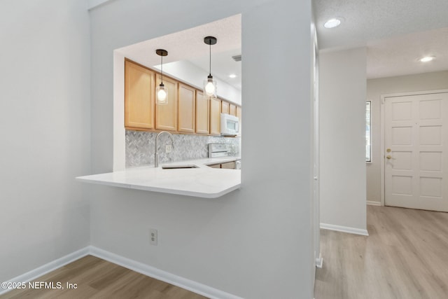 kitchen featuring white appliances, light brown cabinets, sink, backsplash, and hanging light fixtures