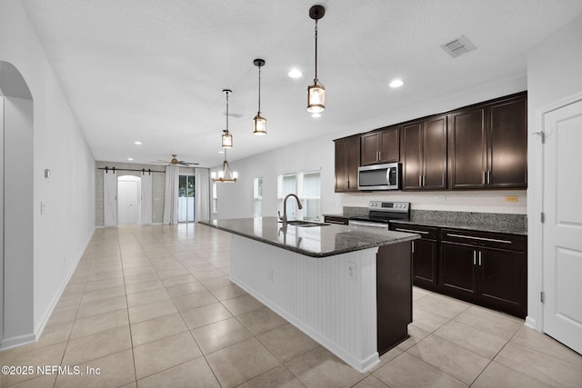 kitchen featuring sink, hanging light fixtures, stainless steel appliances, a barn door, and a kitchen island with sink