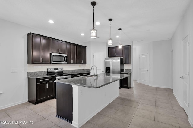 kitchen with dark brown cabinetry, sink, dark stone countertops, appliances with stainless steel finishes, and a kitchen island with sink