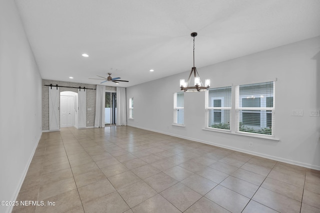 unfurnished room featuring brick wall, light tile patterned flooring, a barn door, and ceiling fan with notable chandelier