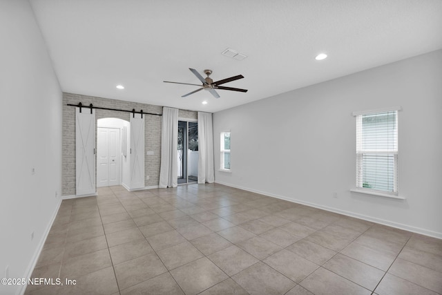 empty room featuring brick wall, light tile patterned flooring, a barn door, and a wealth of natural light