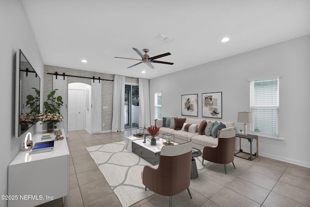 tiled living room with a barn door, ceiling fan, and brick wall