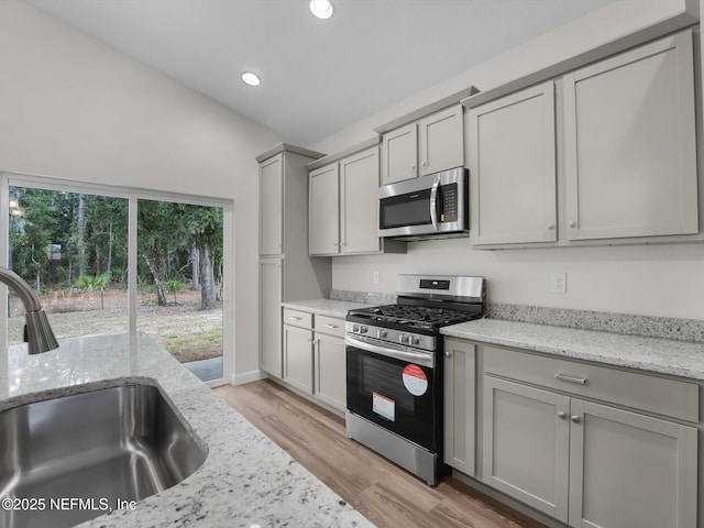 kitchen featuring light hardwood / wood-style flooring, stainless steel appliances, sink, light stone counters, and gray cabinetry