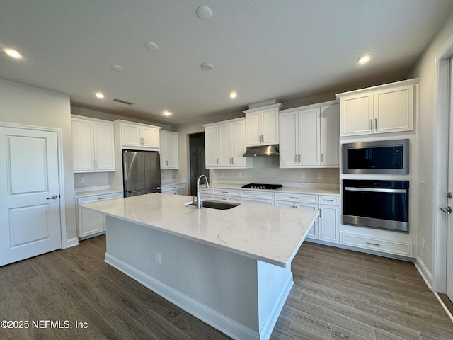 kitchen featuring sink, appliances with stainless steel finishes, light stone counters, an island with sink, and white cabinets