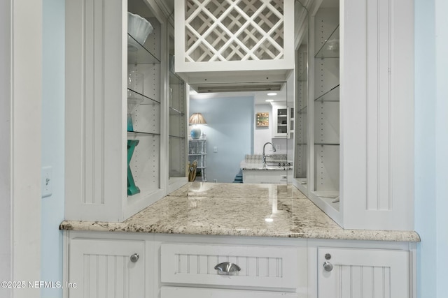 bar with light stone counters, sink, and white cabinetry