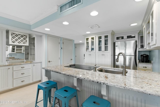 kitchen featuring stainless steel refrigerator, crown molding, light stone countertops, a breakfast bar, and sink