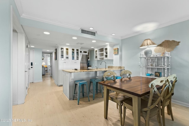 dining area with sink, ornamental molding, and light wood-type flooring