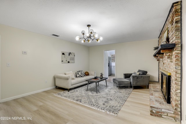 living room with a brick fireplace, a textured ceiling, a notable chandelier, and hardwood / wood-style floors