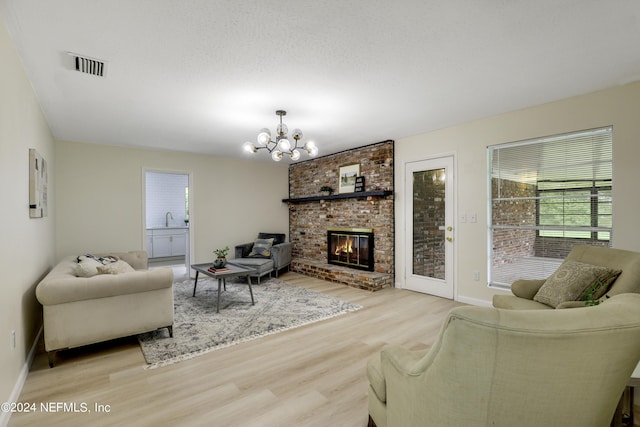 living room featuring a textured ceiling, a fireplace, light wood-type flooring, and an inviting chandelier