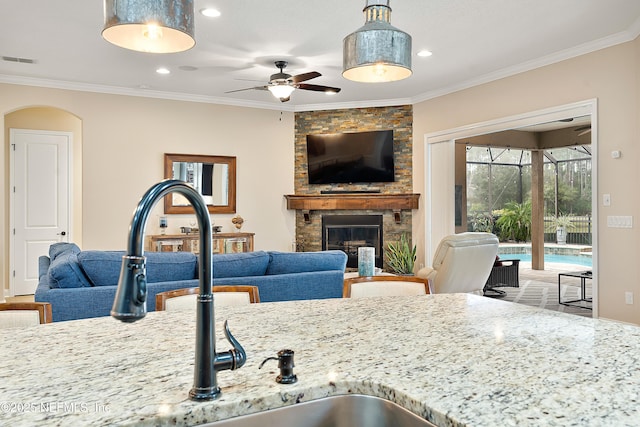 kitchen with crown molding, ceiling fan, light stone counters, and a stone fireplace