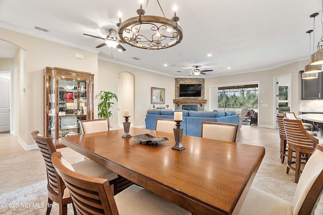 dining space with ceiling fan with notable chandelier, crown molding, a fireplace, and light tile patterned floors