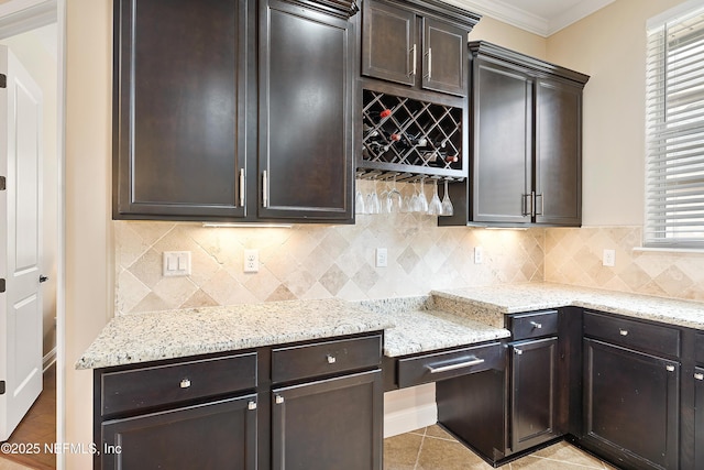 kitchen featuring light stone counters, light tile patterned floors, crown molding, and dark brown cabinetry