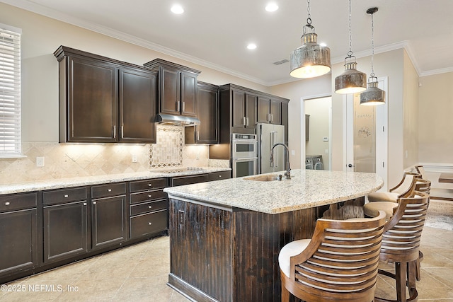 kitchen featuring hanging light fixtures, a center island with sink, a breakfast bar, tasteful backsplash, and sink