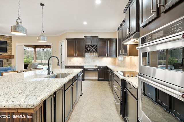 kitchen with light stone countertops, hanging light fixtures, a center island with sink, stainless steel double oven, and sink