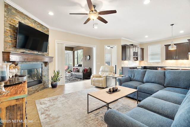 tiled living room featuring a large fireplace, ceiling fan, and crown molding