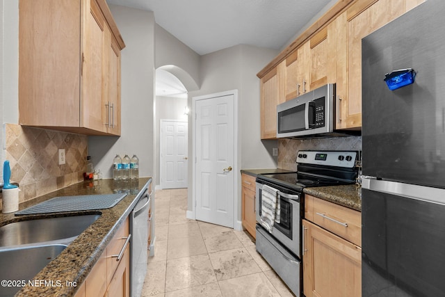 kitchen featuring backsplash, dark stone countertops, light brown cabinets, and stainless steel appliances