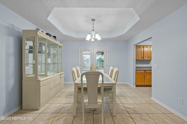 dining area featuring a textured ceiling, a raised ceiling, an inviting chandelier, and light tile patterned floors