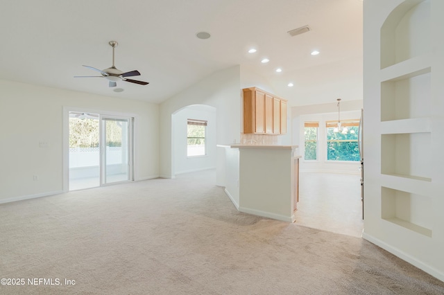 unfurnished living room with built in shelves, ceiling fan, a healthy amount of sunlight, and light carpet