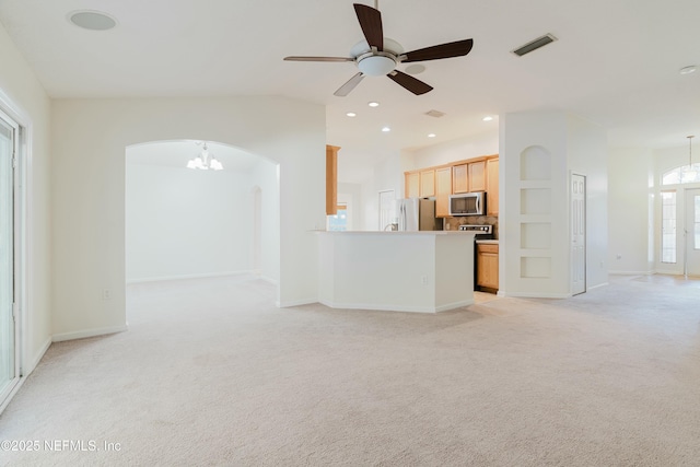 unfurnished living room featuring ceiling fan with notable chandelier, light colored carpet, and plenty of natural light