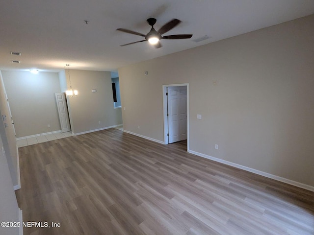 unfurnished room with ceiling fan with notable chandelier and light hardwood / wood-style flooring