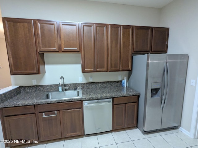 kitchen with sink, light tile patterned floors, dark stone counters, and appliances with stainless steel finishes