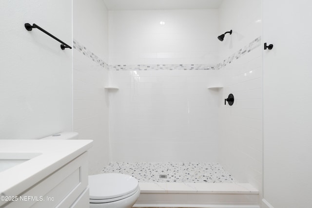 bathroom featuring a tile shower, toilet, and vanity