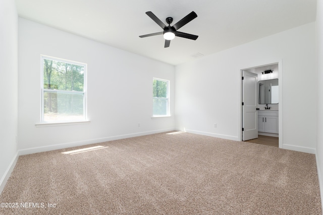 unfurnished bedroom featuring ceiling fan, light colored carpet, and ensuite bath