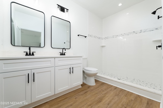 bathroom featuring wood-type flooring, toilet, vanity, and a shower