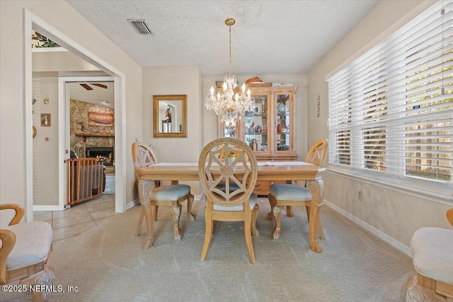 dining area with a notable chandelier, light carpet, a stone fireplace, and a textured ceiling